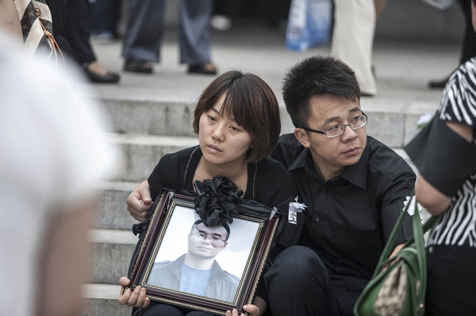 2012年7月25日,在北京广渠门桥下遇难的驾车人丁志健的追悼会在八宝山举行,亲友同事赶来为他送行。图为丁的妻子怀捧遗像,神情绝望。